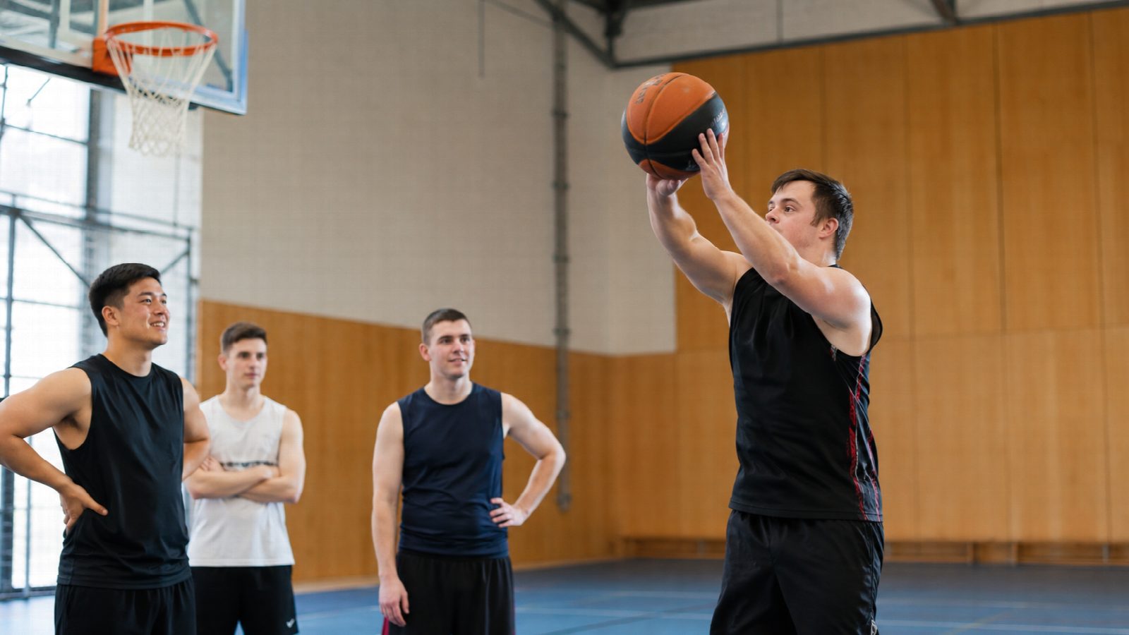 Junger Basketballspieler mit Down-Syndrom wirft auf den Korb, Mitspieler schauen zu