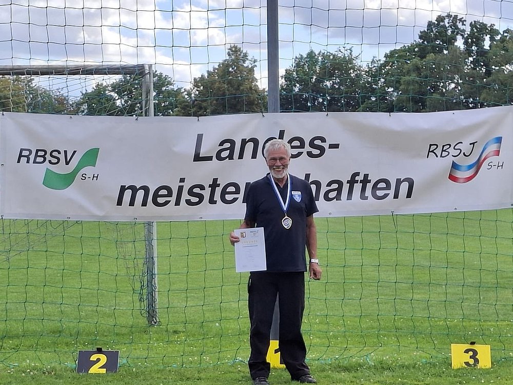 Ein Sportler mit Medaille und Urkunde auf Platz 1 vor dem Banner der Landesmeisterschaften.