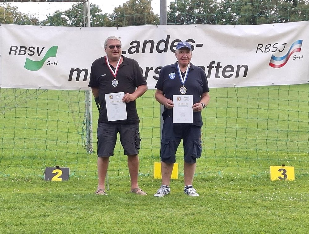 Zwei Sportler mit Medaillen und Urkunden vor dem Banner der Landesmeisterschaften, daneben die Platzierungsschilder 2 und 3.