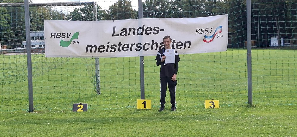 Ein Jugendlicher in schwarzem Trainingsanzug hält seine Urkunde auf Platz 1 vor dem Banner der Landesmeisterschaften.